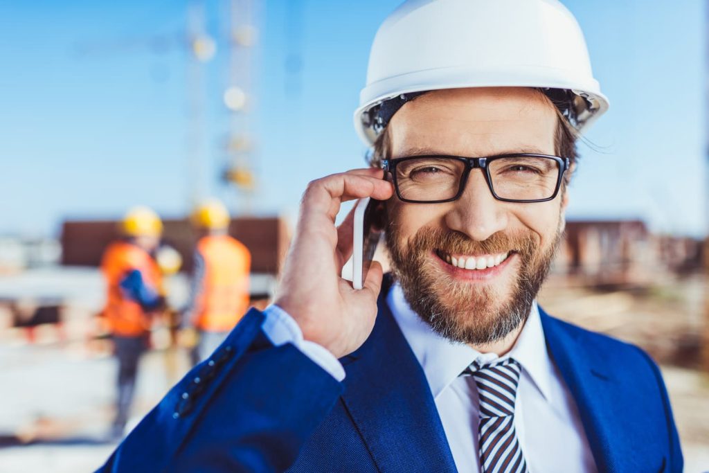 Homme d'affaires en casque et costume parlant au téléphone tout en se tenant debout sur le chantier